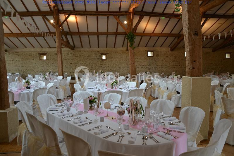 Salle de réception décorée avec des tables rondes, nappes blanches, chemins de table roses et chaises habillées.