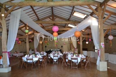 Vue depuis une porte vitrée sur un jardin avec des tables hautes et des chaises disposées près d'un bâtiment en pierre.