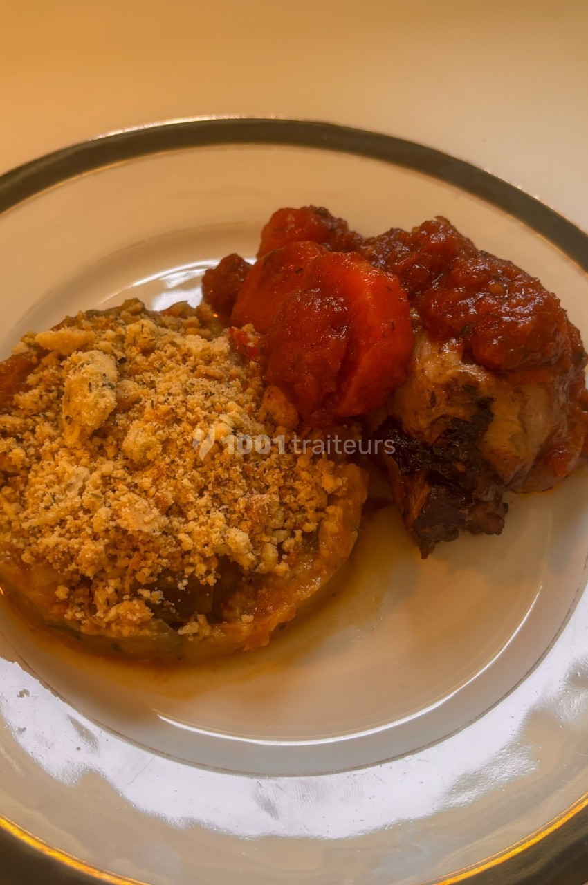 Assiette contenant un gratin de légumes avec une chapelure dorée et un morceau de viande en sauce tomate.