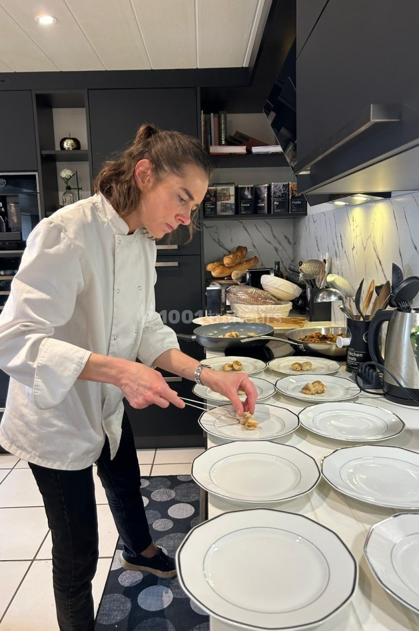 Une chef prépare des assiettes dans une cuisine moderne avec des plats et ustensiles disposés autour.