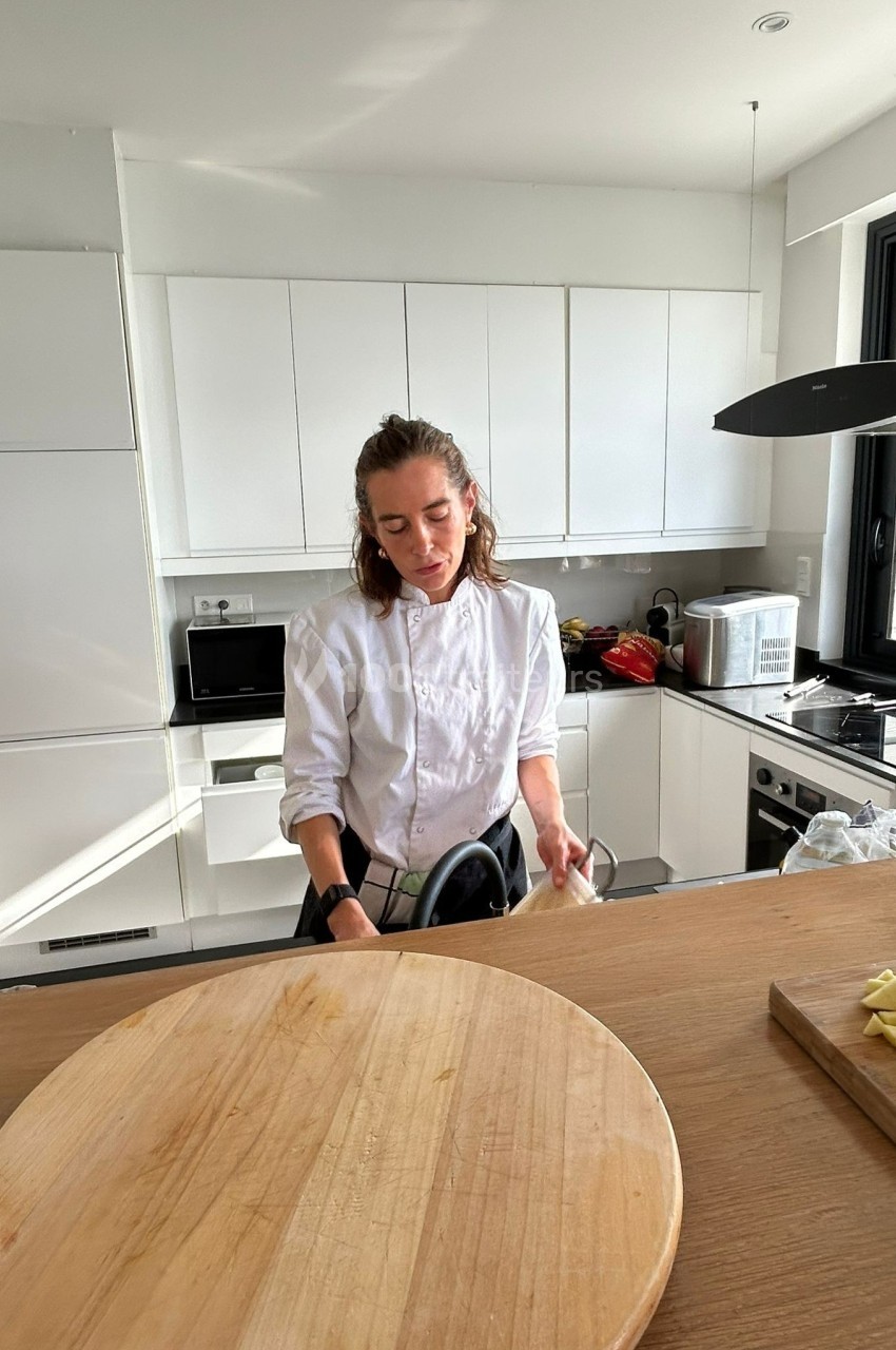 Une femme en tenue de chef cuisine dans une cuisine moderne avec un plan de travail en bois.