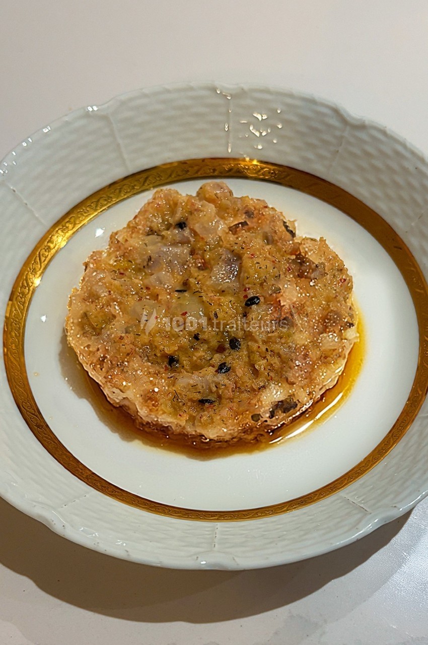 Tartare de poisson présenté dans une assiette blanche bordée d'un motif doré, avec une sauce légère.