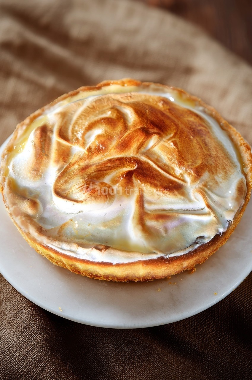 Tartelette meringuée dorée posée sur une assiette blanche, avec un fond en tissu brun.