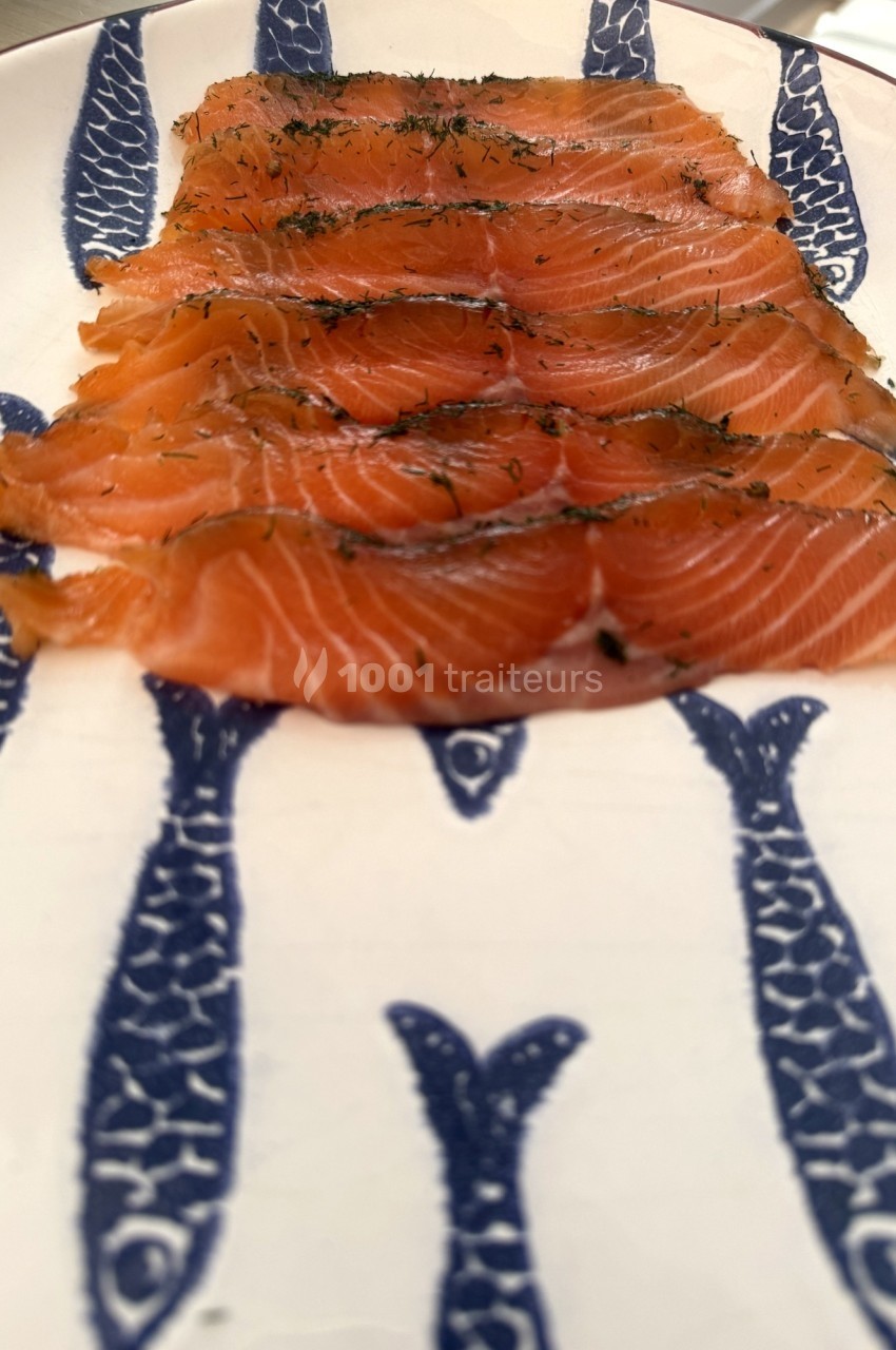 Tranches de saumon fumé garnies d'aneth, disposées sur une assiette décorée de motifs de poissons bleus.