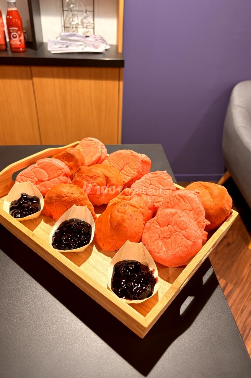 Plateau de petits pains roses accompagnés de confiture de fruits rouges dans des coupelles en bois.