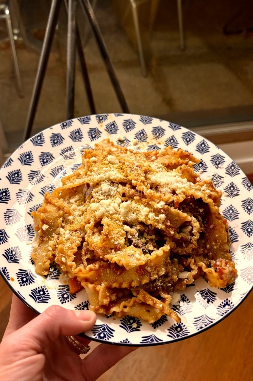Assiette de pâtes à la sauce tomate garnies de fromage râpé, tenue à la main dans un intérieur éclairé.