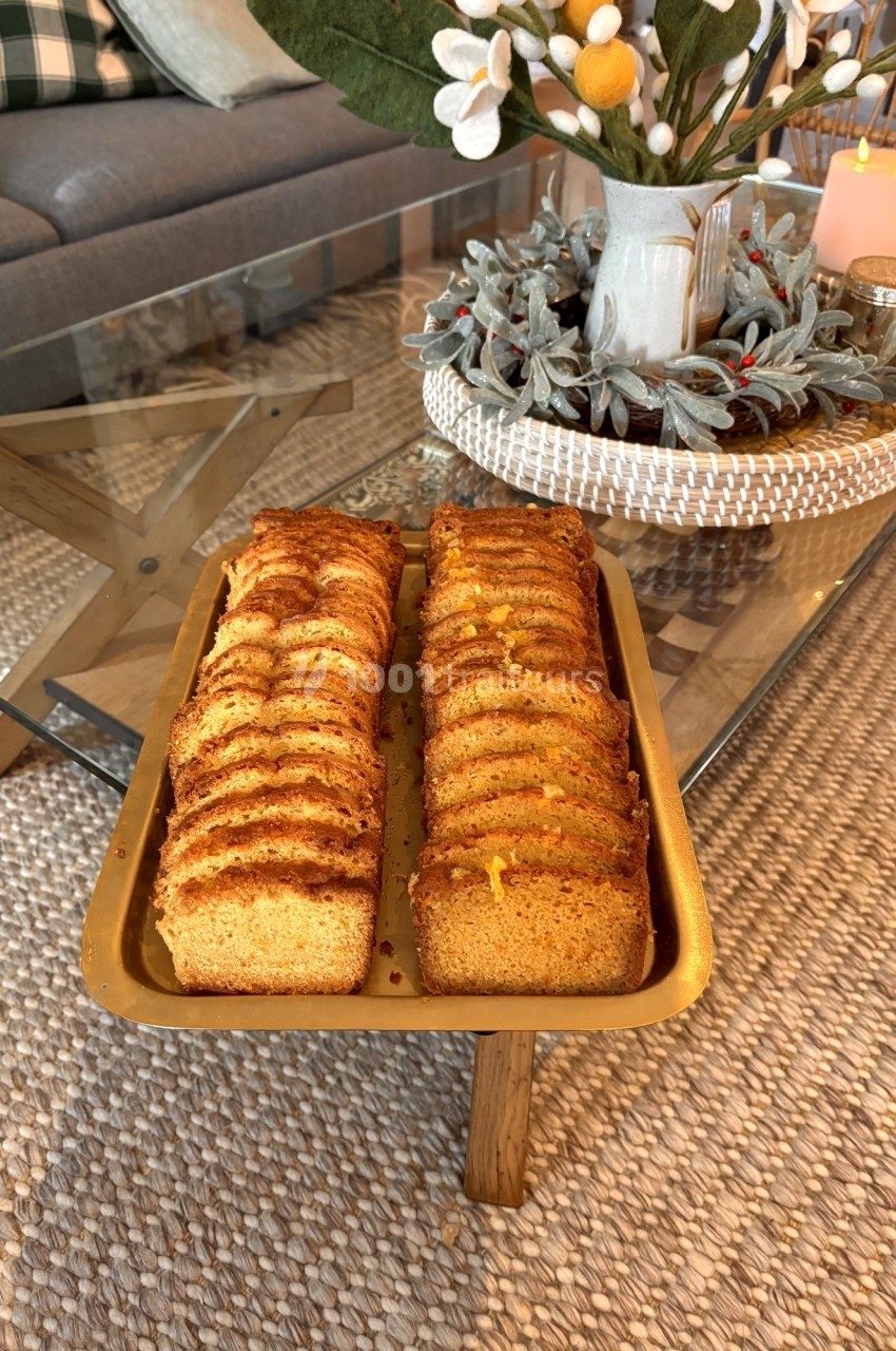 Tranches de cake dorées disposées sur un plateau doré, posé sur une table basse en verre dans un salon décoré.