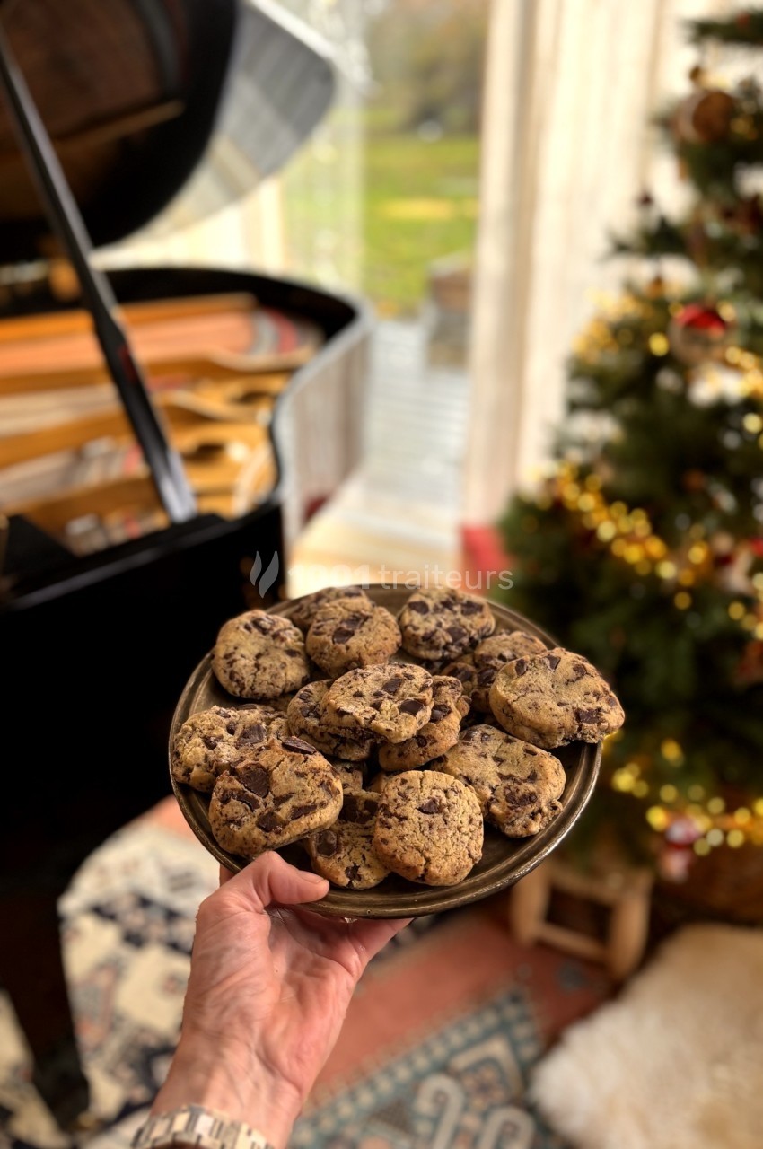 Assiette de cookies aux pépites de chocolat tenue devant un piano et un sapin de Noël décoré.