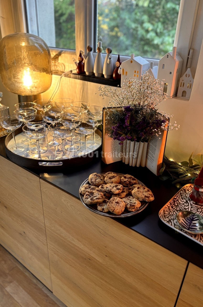 Buffet décoré avec des coupes en verre, des biscuits, des fleurs séchées et des figurines devant une fenêtre.