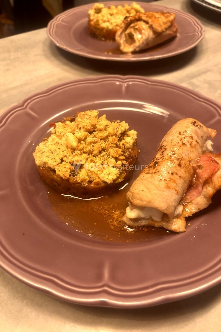Assiette contenant un roulé de viande farci et une tomate garnie de crumble salé, servie sur une assiette violette.