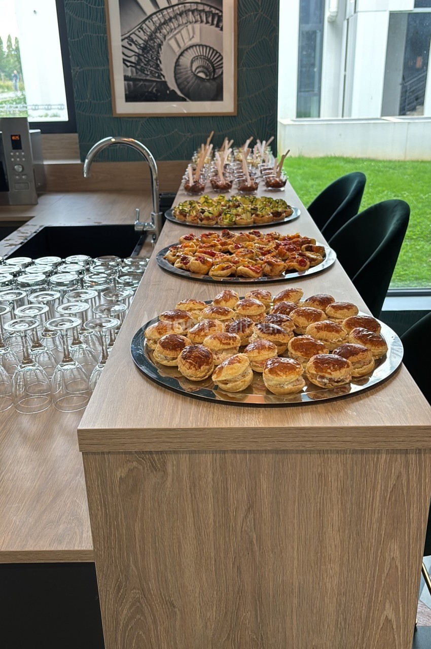Plateaux de bouchées salées et sucrées disposés sur un comptoir en bois, avec des verres alignés à côté.