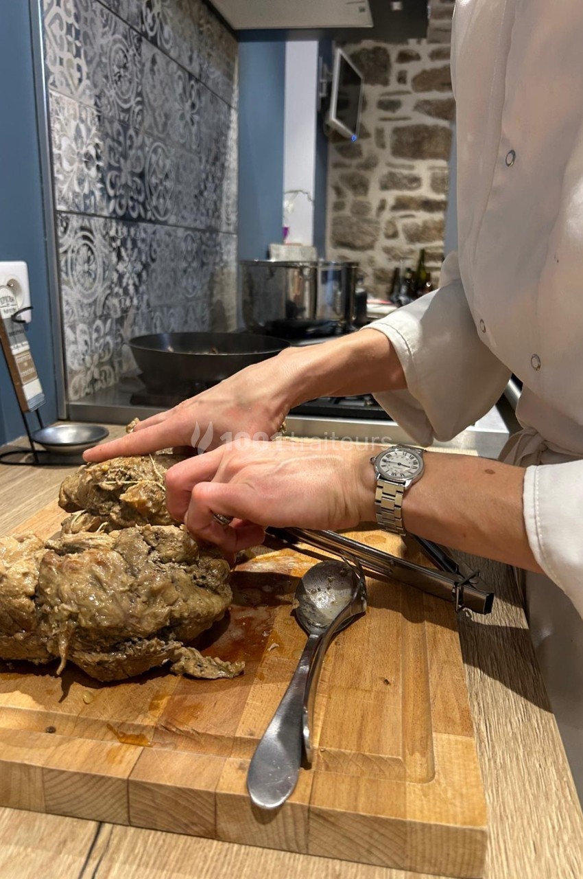 Une personne découpe un morceau de viande cuite sur une planche en bois dans une cuisine au décor rustique.