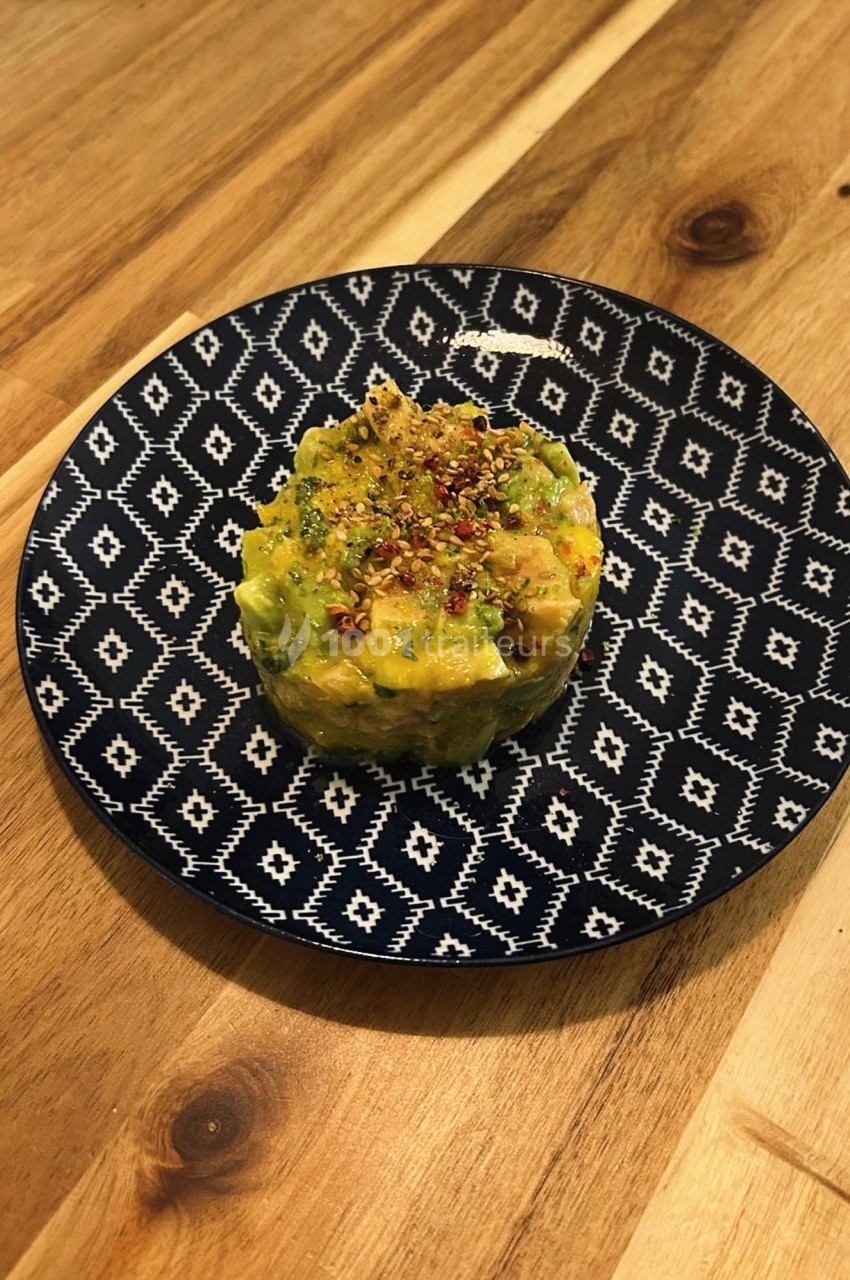 Tartare d'avocat et mangue, assaisonné et présenté sur une assiette à motifs géométriques.