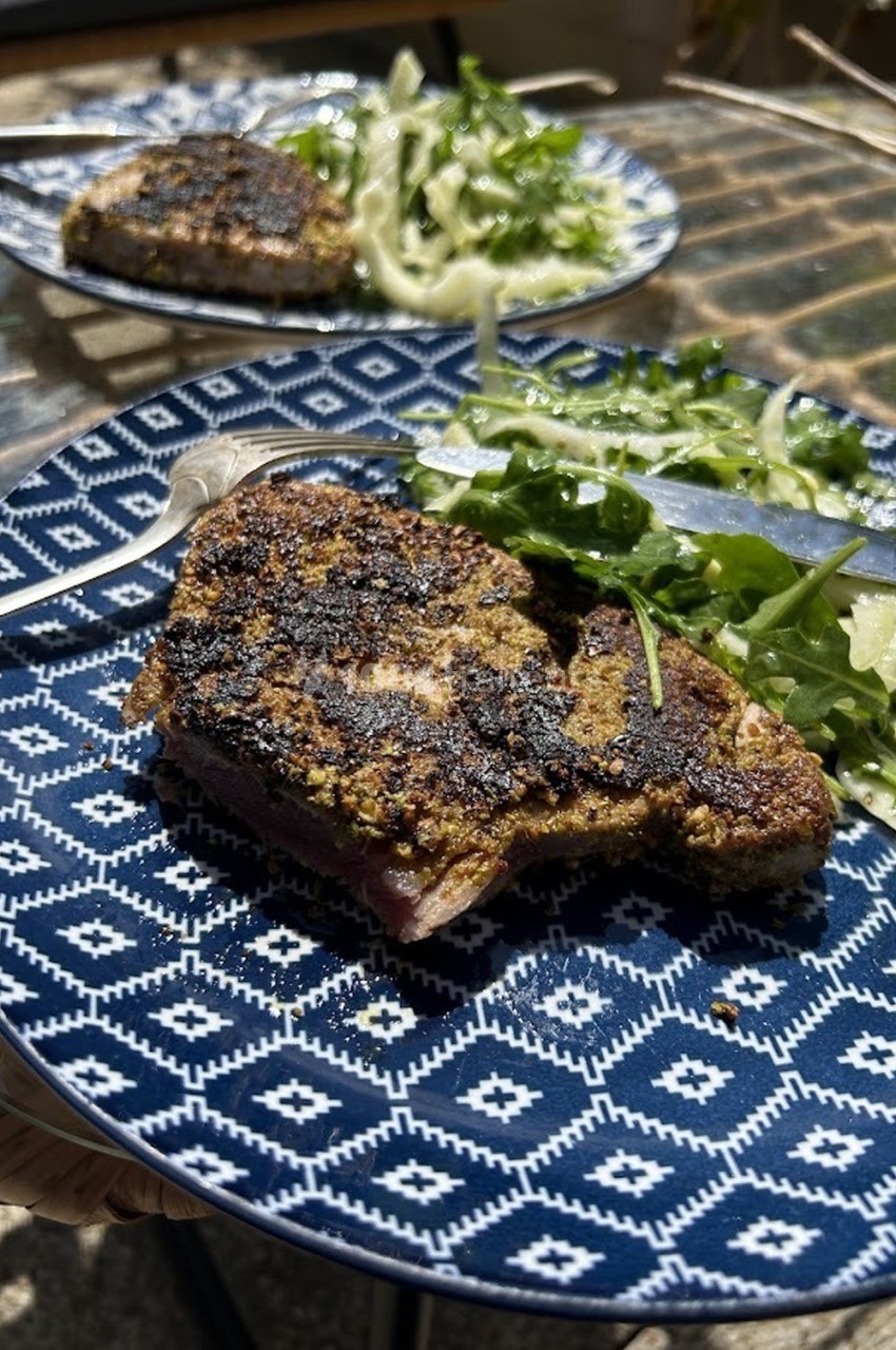 Assiette contenant un steak grillé accompagné de salade verte et de fenouil, posée sur une table en extérieur.