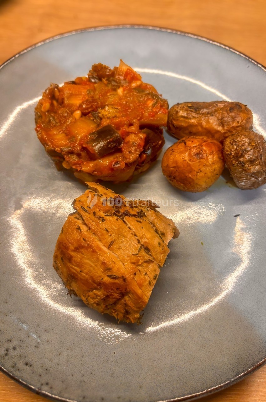 Assiette contenant un morceau de viande, des pommes de terre rôties et une portion de ratatouille.