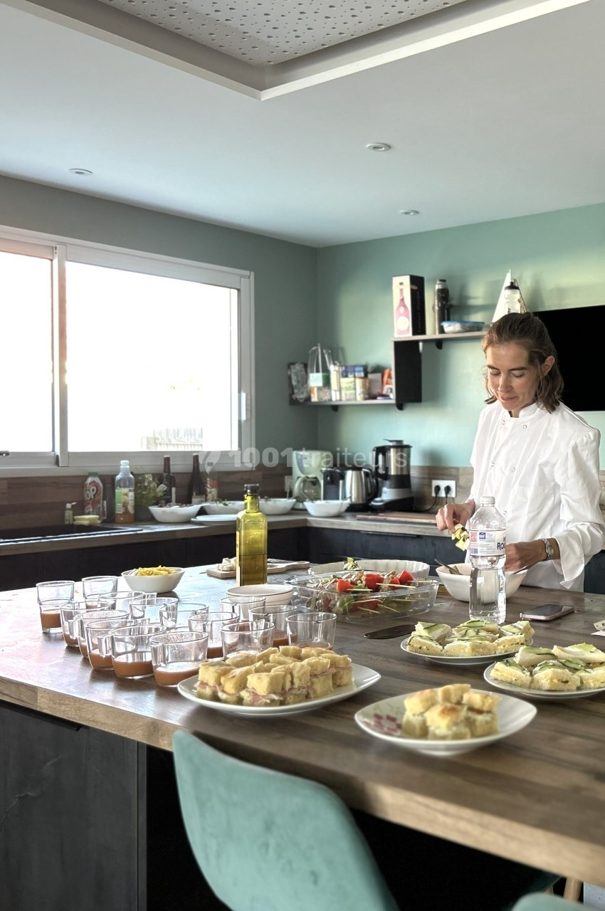 Une femme prépare des plats dans une cuisine moderne avec des assiettes de nourriture et des verres disposés sur un îlot…