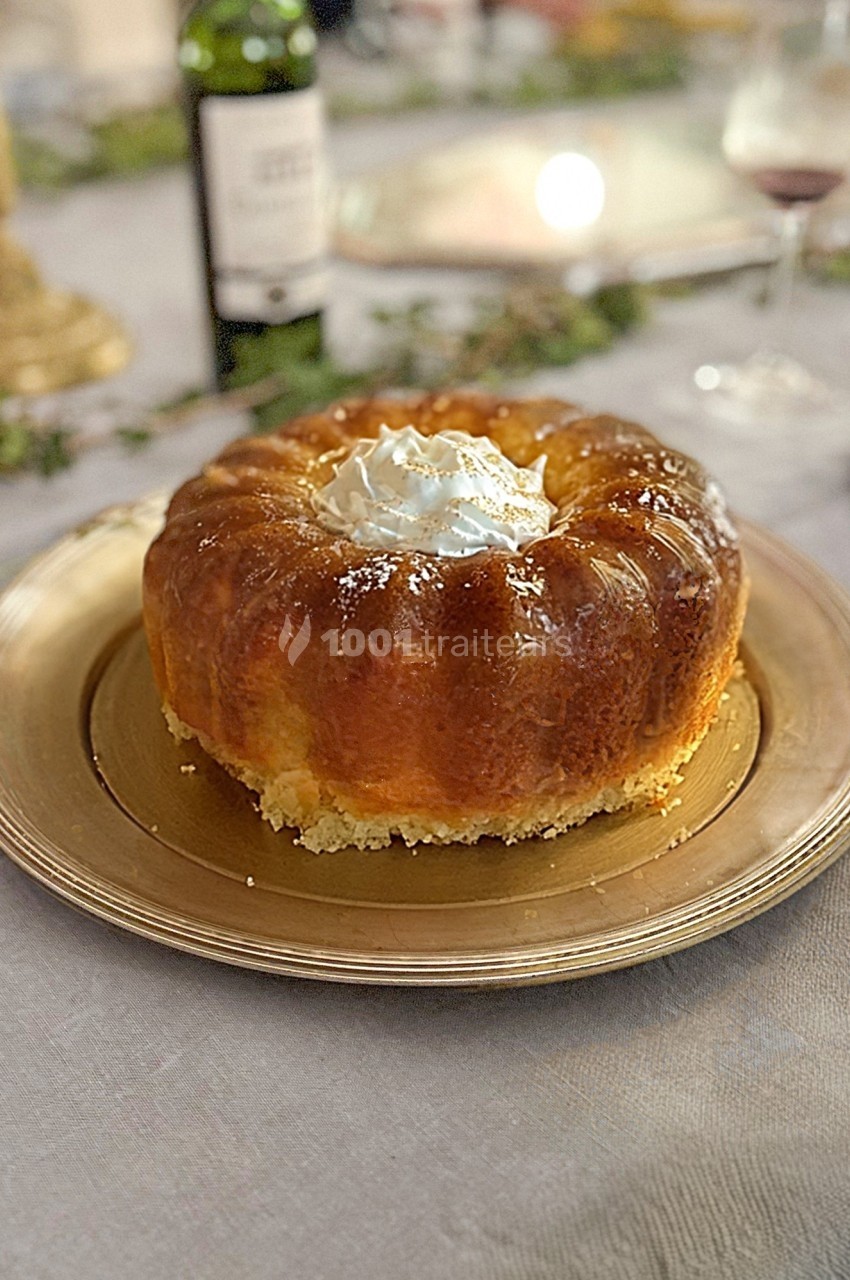 Gâteau baba au rhum garni de crème fouettée, présenté sur une assiette dorée sur une table dressée.