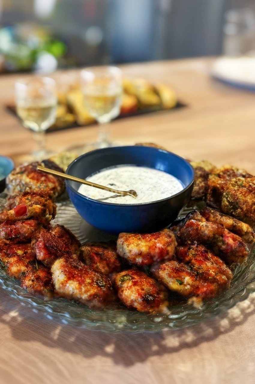 Assiette de boulettes de viande grillées entourant un bol de sauce blanche, servie sur une table en bois.