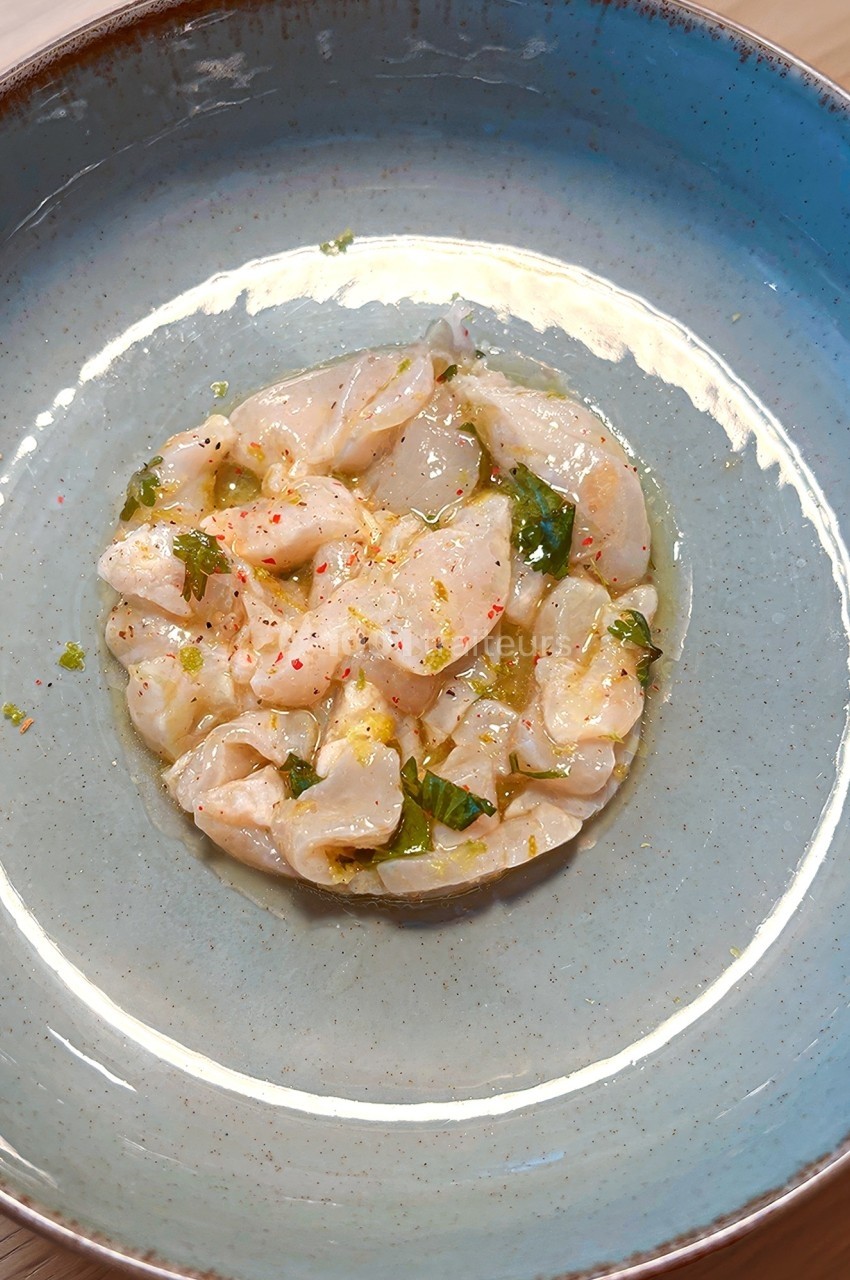 Carpaccio de poisson cru assaisonné avec des herbes et des épices, présenté dans une assiette bleue.