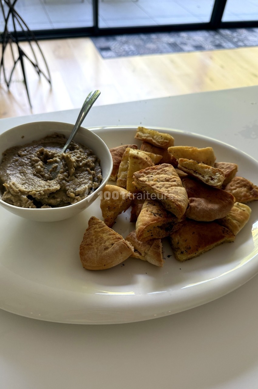 Assiette avec un bol de houmous et des morceaux de pain pita grillés sur une table blanche.