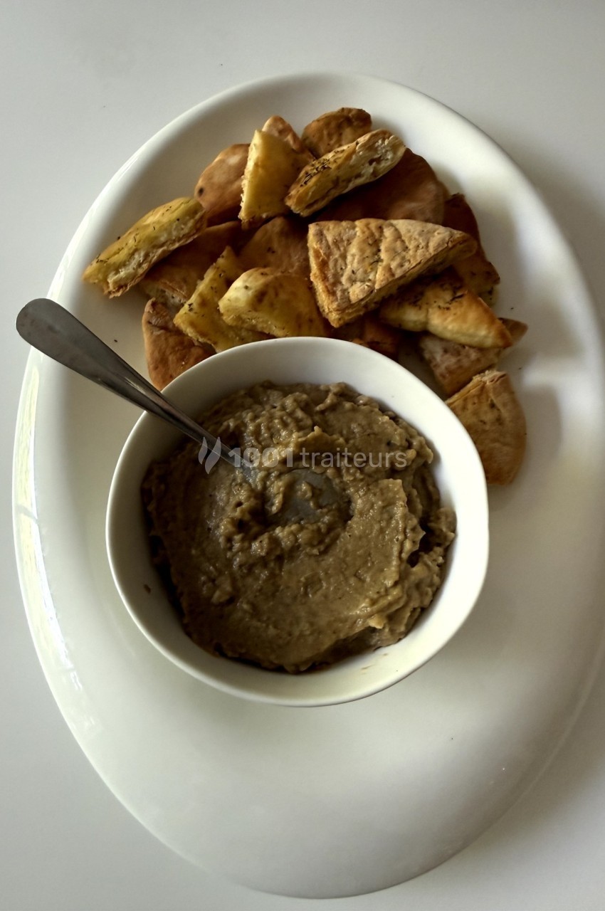 Bol de houmous accompagné de morceaux de pain pita grillés, disposés sur une assiette blanche.