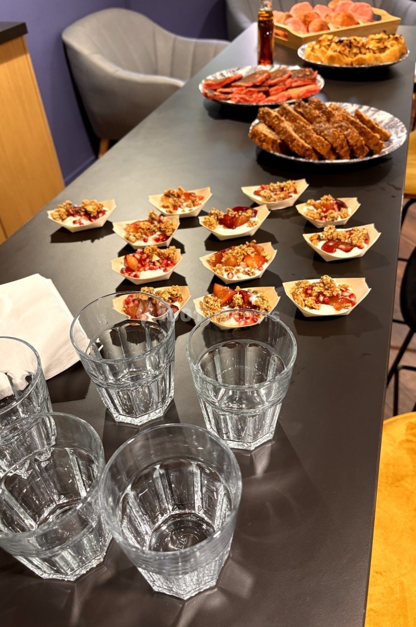 Table avec des verrines de fruits, des plats de viande et des verres en verre, dans un espace de restauration.