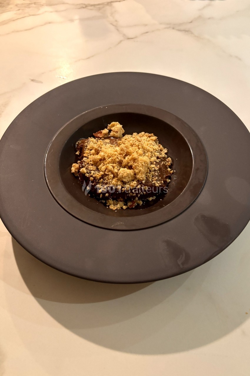 Dessert servi dans une assiette noire, composé d'une base chocolatée et recouvert d'un crumble doré.