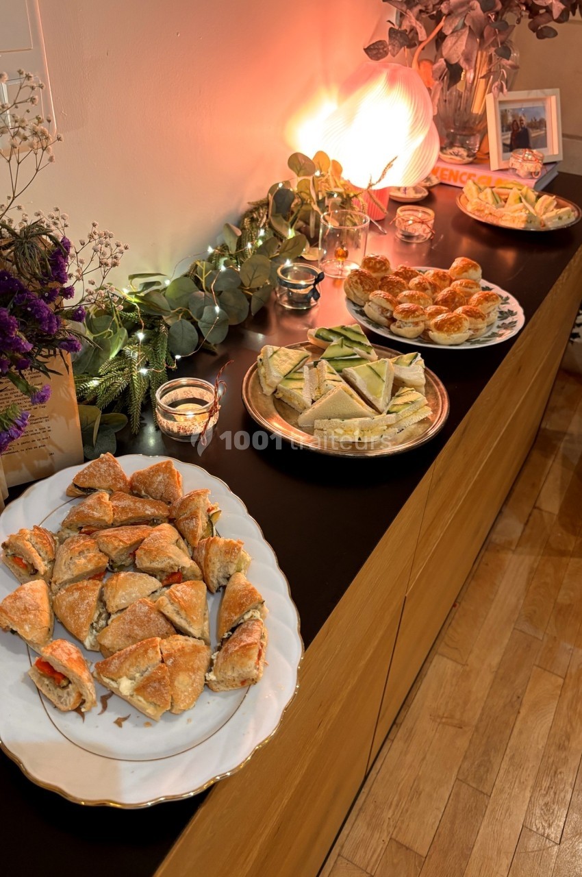 Plats variés de sandwichs et amuse-bouches disposés sur un buffet décoré de lumières et de feuillages.
