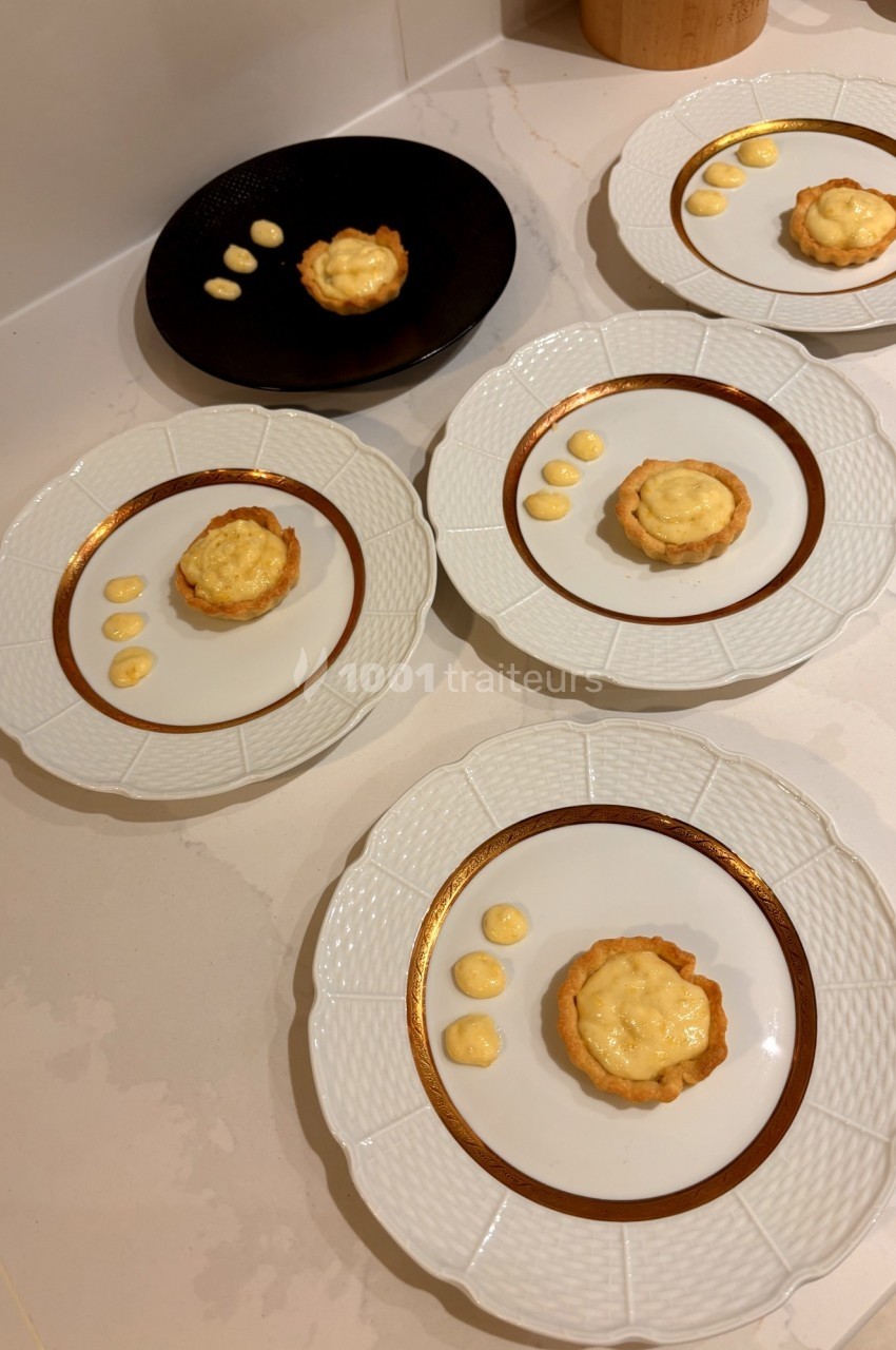 Tartelettes individuelles au citron disposées sur des assiettes blanches et noires, décorées de points de crème.