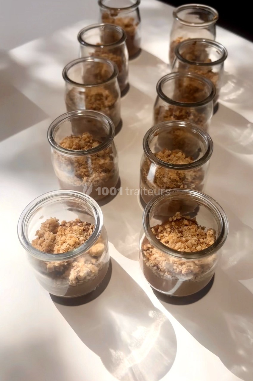 Petits pots en verre alignés contenant un dessert avec une base crémeuse et un crumble doré sur le dessus.