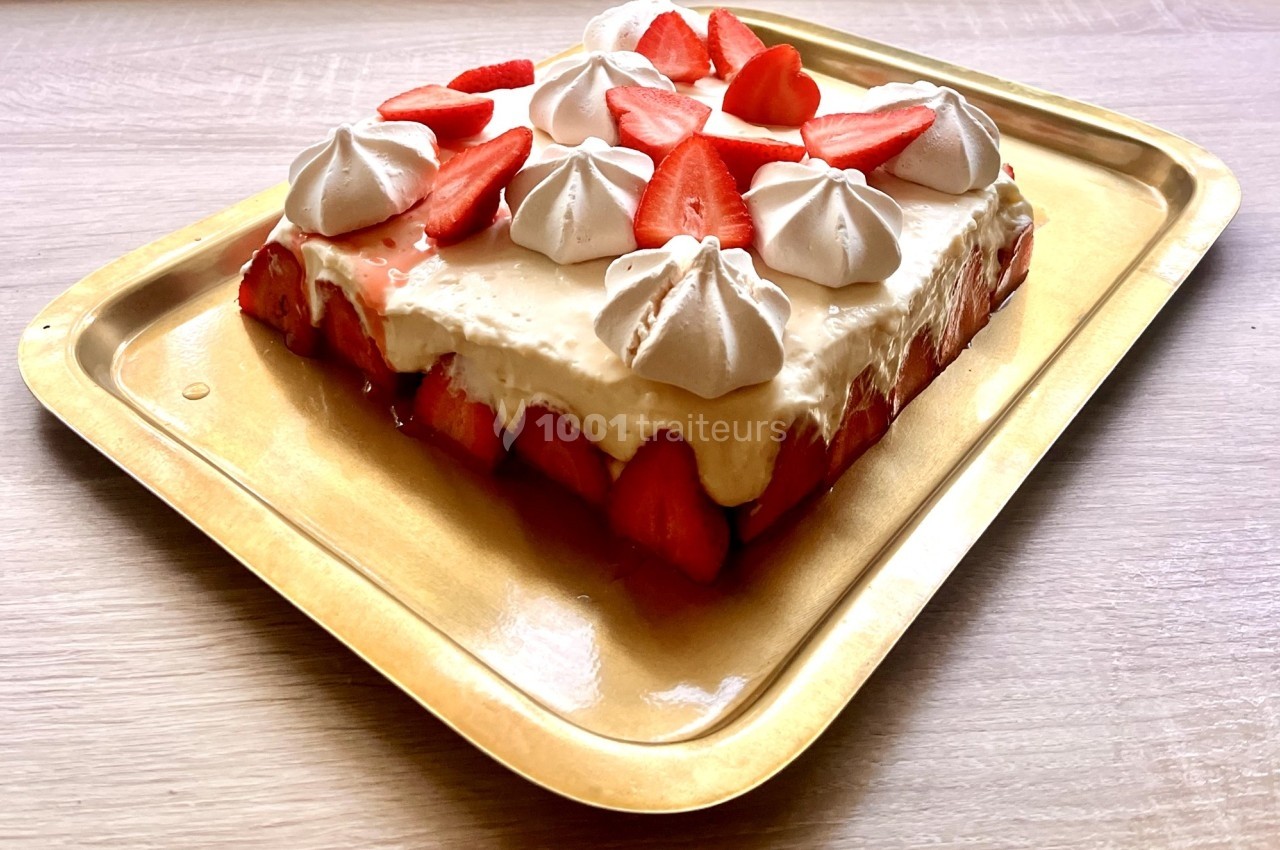 Gâteau rectangulaire garni de fraises fraîches, de crème et de meringues, présenté sur un plateau doré.
