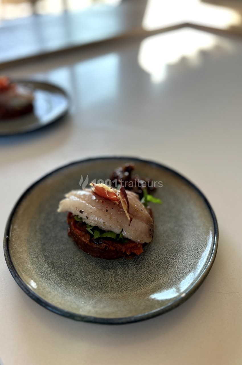 Assiette contenant une tranche de poisson sur un lit de légumes et pain grillé, présentée sur une table lumineuse.