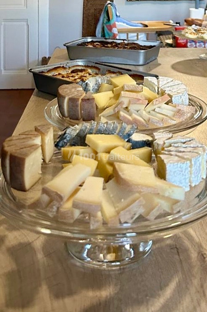 Plateaux de fromages variés disposés sur des présentoirs en verre, avec des plats en arrière-plan sur une table en bois.