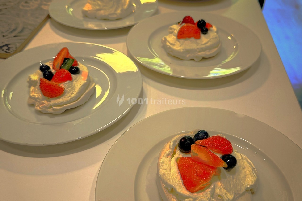 Assiettes de pavlovas individuelles garnies de fraises, myrtilles et crème sur une table blanche.