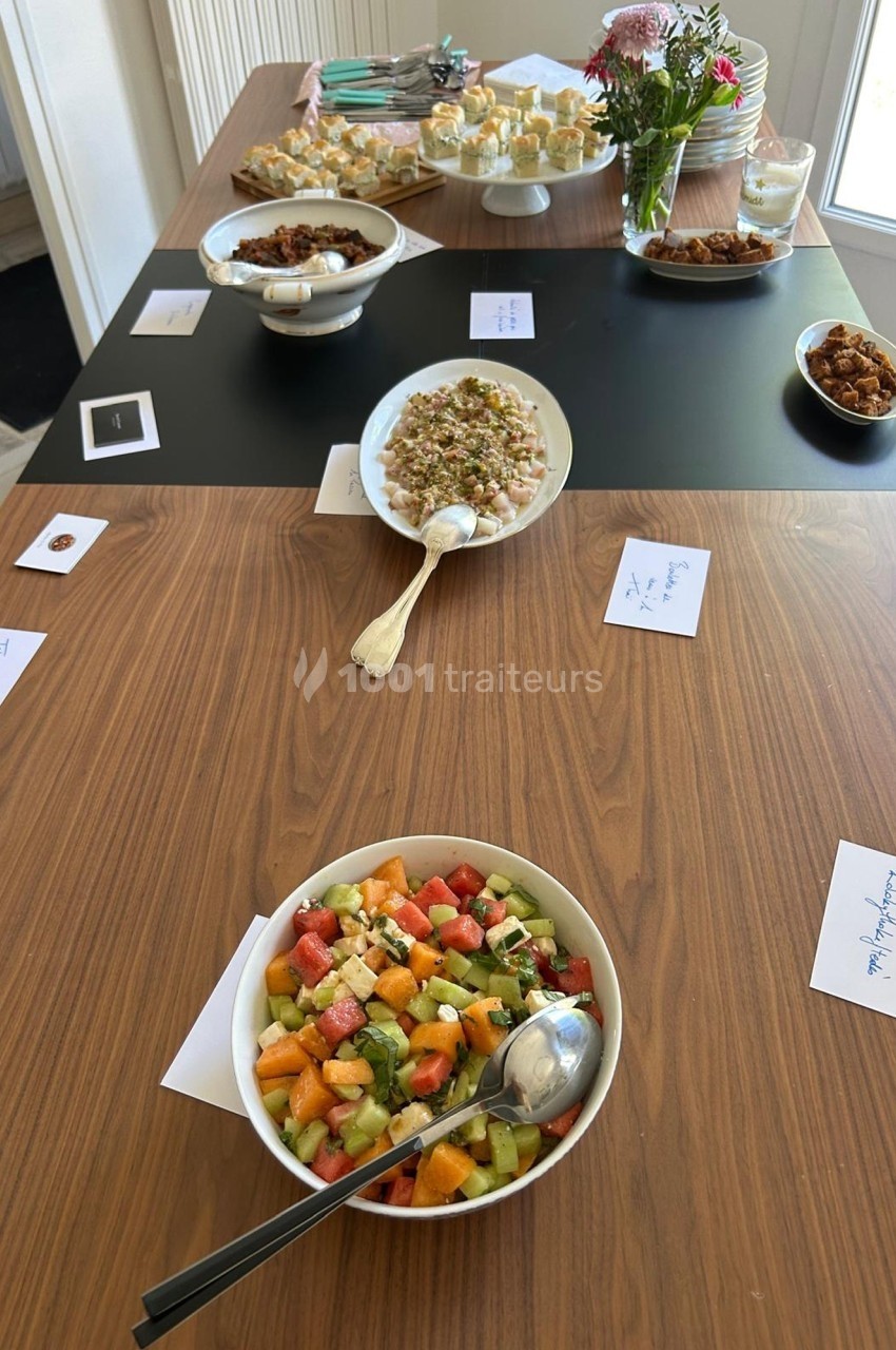Table en bois avec divers plats, dont une salade de fruits, des desserts et des mets salés, accompagnés de petites…