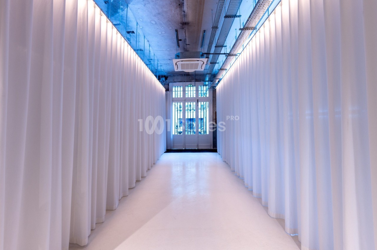 Couloir lumineux avec des rideaux blancs de chaque côté et une grande fenêtre au fond.