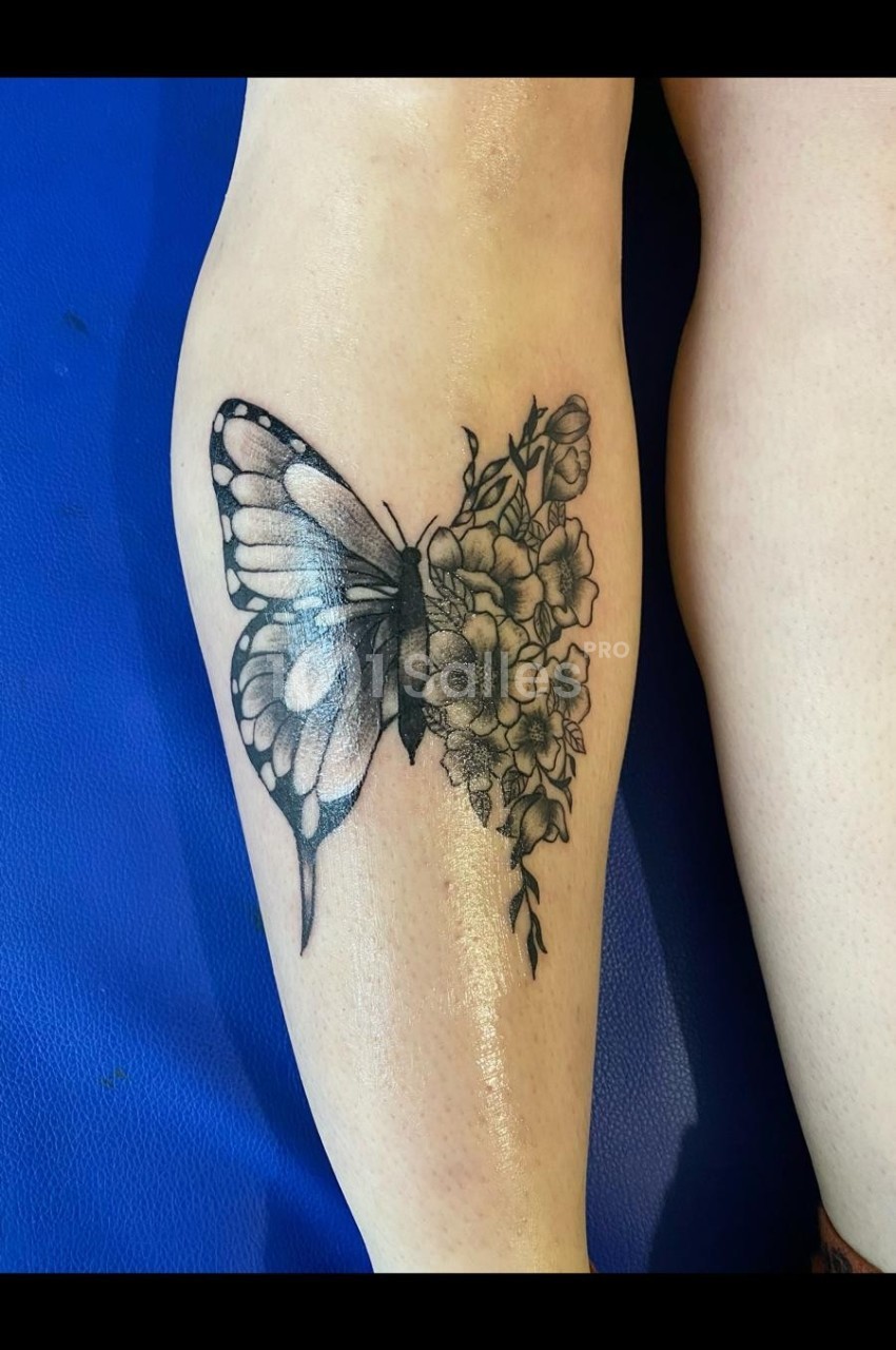Tatouage noir et gris sur une jambe représentant un papillon fusionné avec des fleurs détaillées.