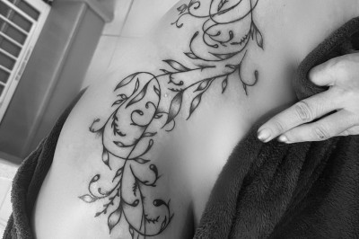 Tatouage floral noir et gris sur une cuisse, représentant des fleurs et des feuilles avec des détails délicats.