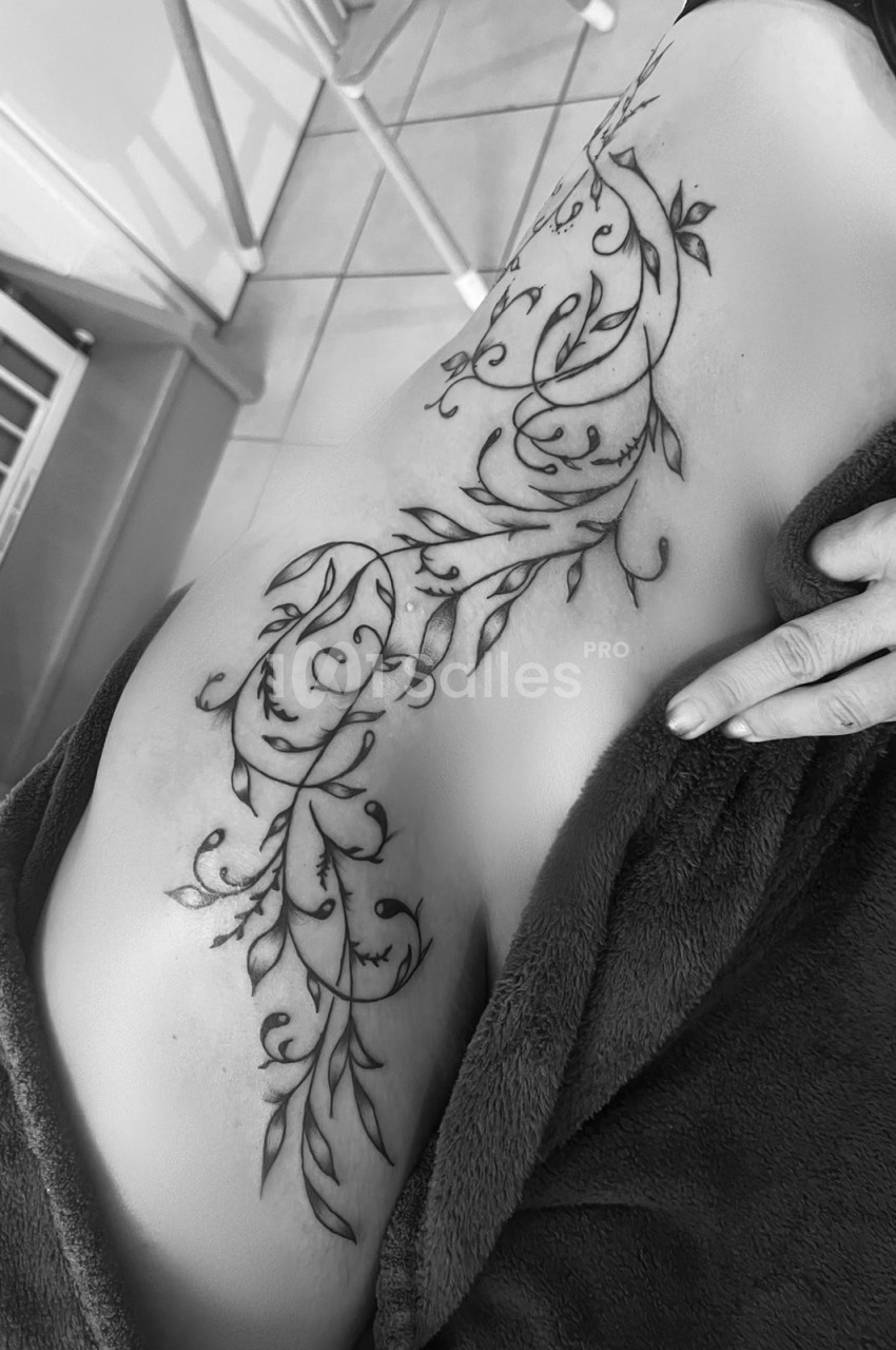 Tatouage floral détaillé couvrant le flanc d'une personne, avec des motifs de feuilles et de courbes élégantes.