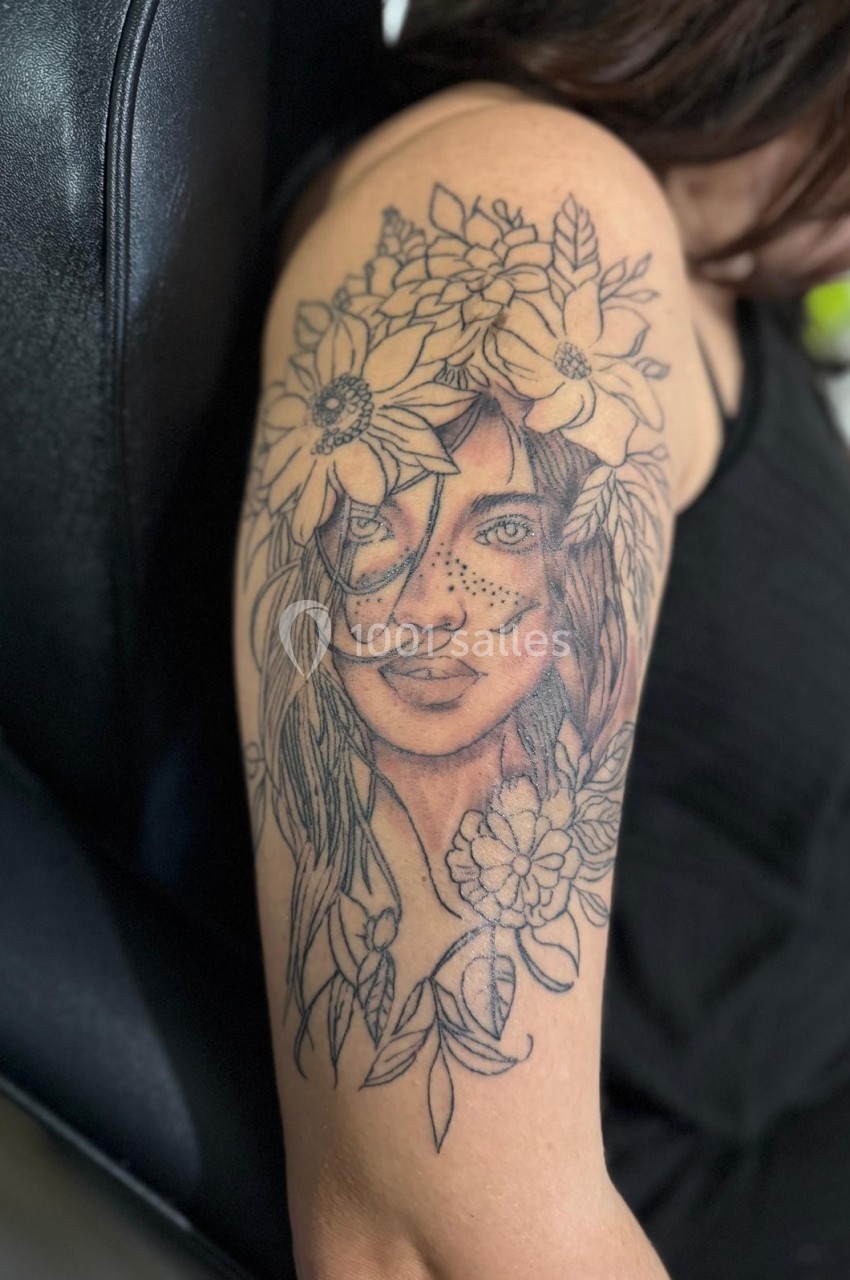 Tatouage détaillé sur le bras représentant un visage féminin entouré de fleurs et de feuilles.