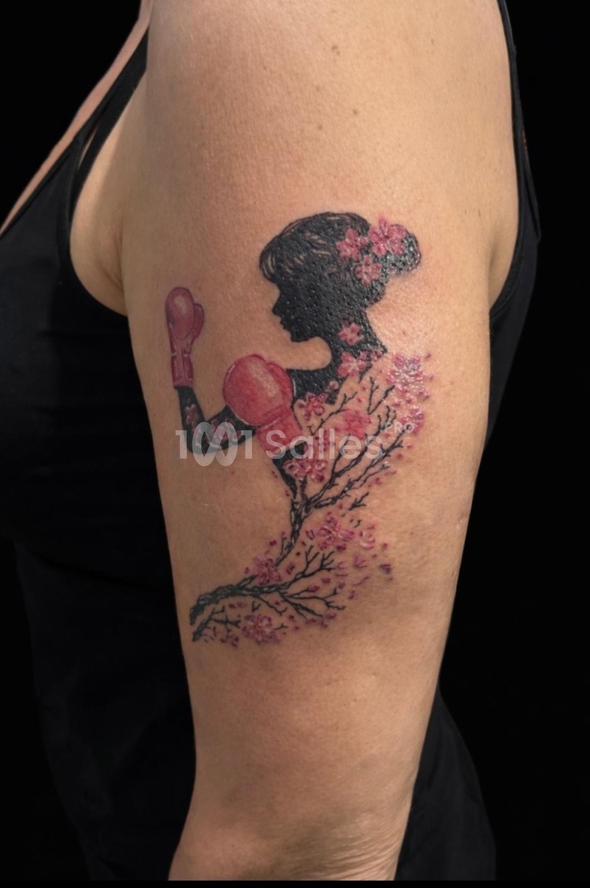Tatouage sur le bras représentant une silhouette féminine avec des gants de boxe et des motifs de fleurs de cerisier.