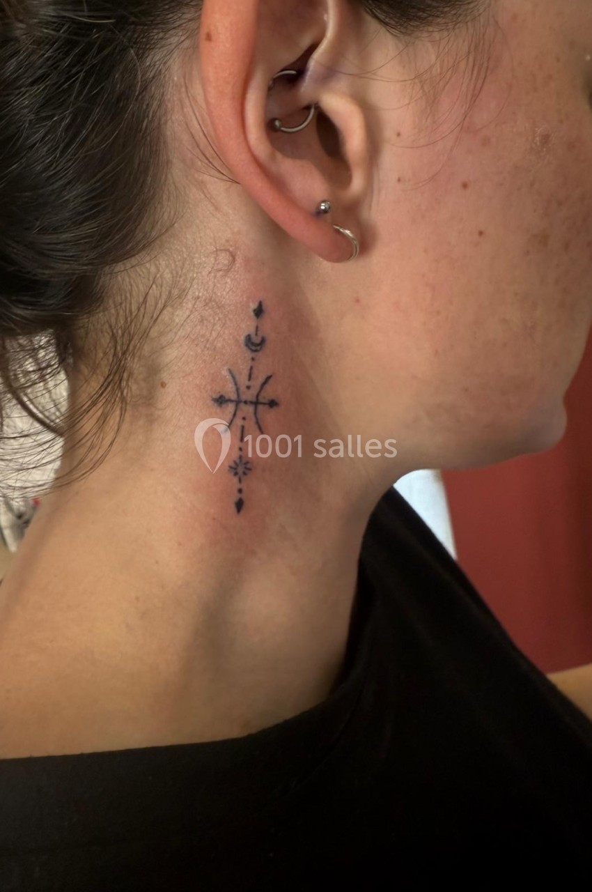 Tatouage minimaliste noir avec motifs géométriques et symboles sur le côté du cou d'une femme.