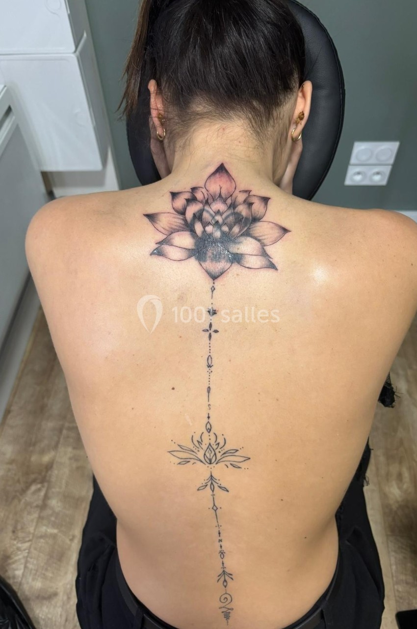 Femme de dos avec un tatouage détaillé représentant une fleur de lotus et des motifs alignés le long de la colonne…