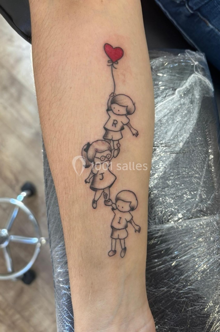 Tatouage sur un avant-bras représentant trois enfants se tenant la main, le premier tenant un ballon en forme de cœur.