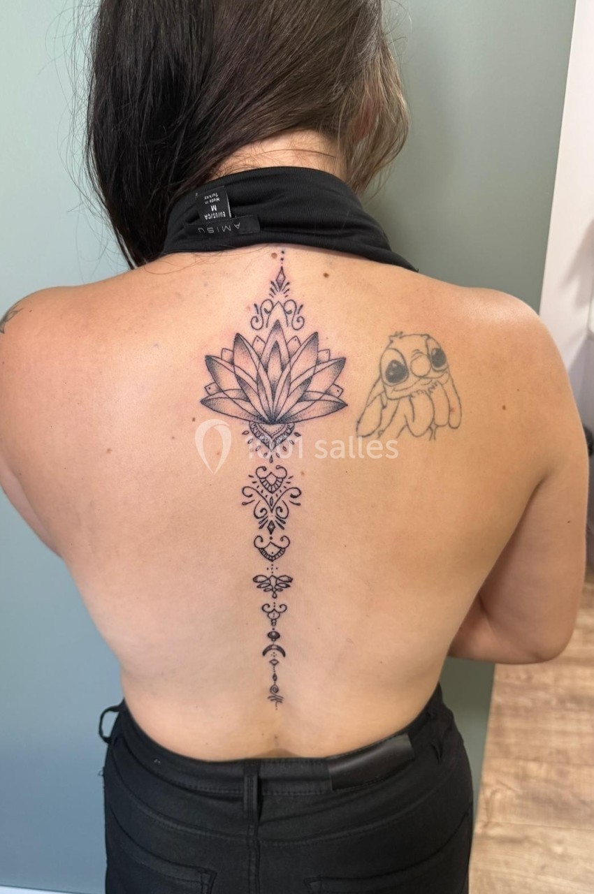 Femme de dos montrant un tatouage floral et géométrique le long de la colonne vertébrale, avec un dessin d'animal sur l…