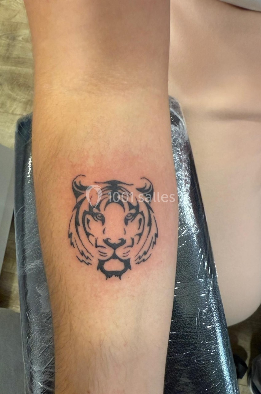 Tatouage noir d'une tête de tigre sur l'avant-bras d'une personne, réalisé sur une peau légèrement rouge.