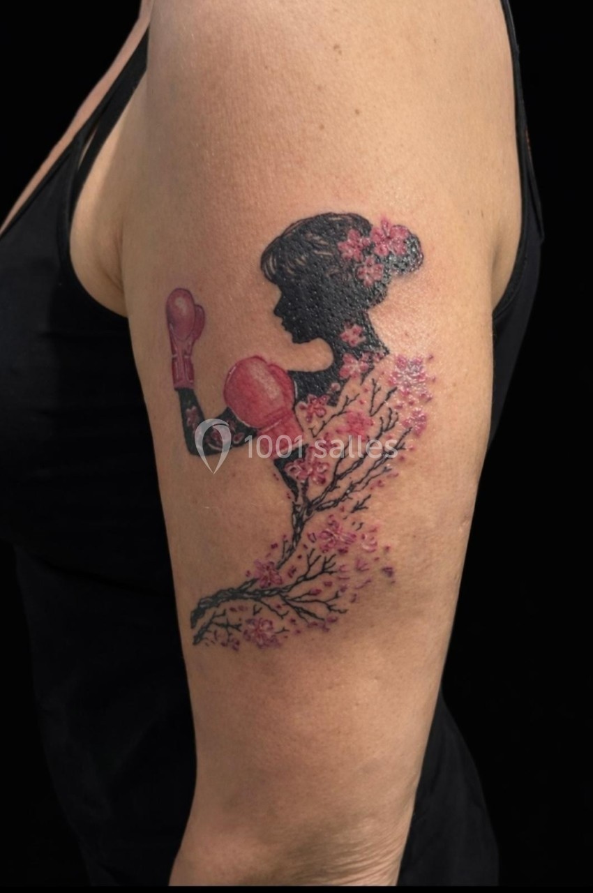 Tatouage sur le bras représentant une silhouette féminine avec des gants de boxe et des fleurs de cerisier.