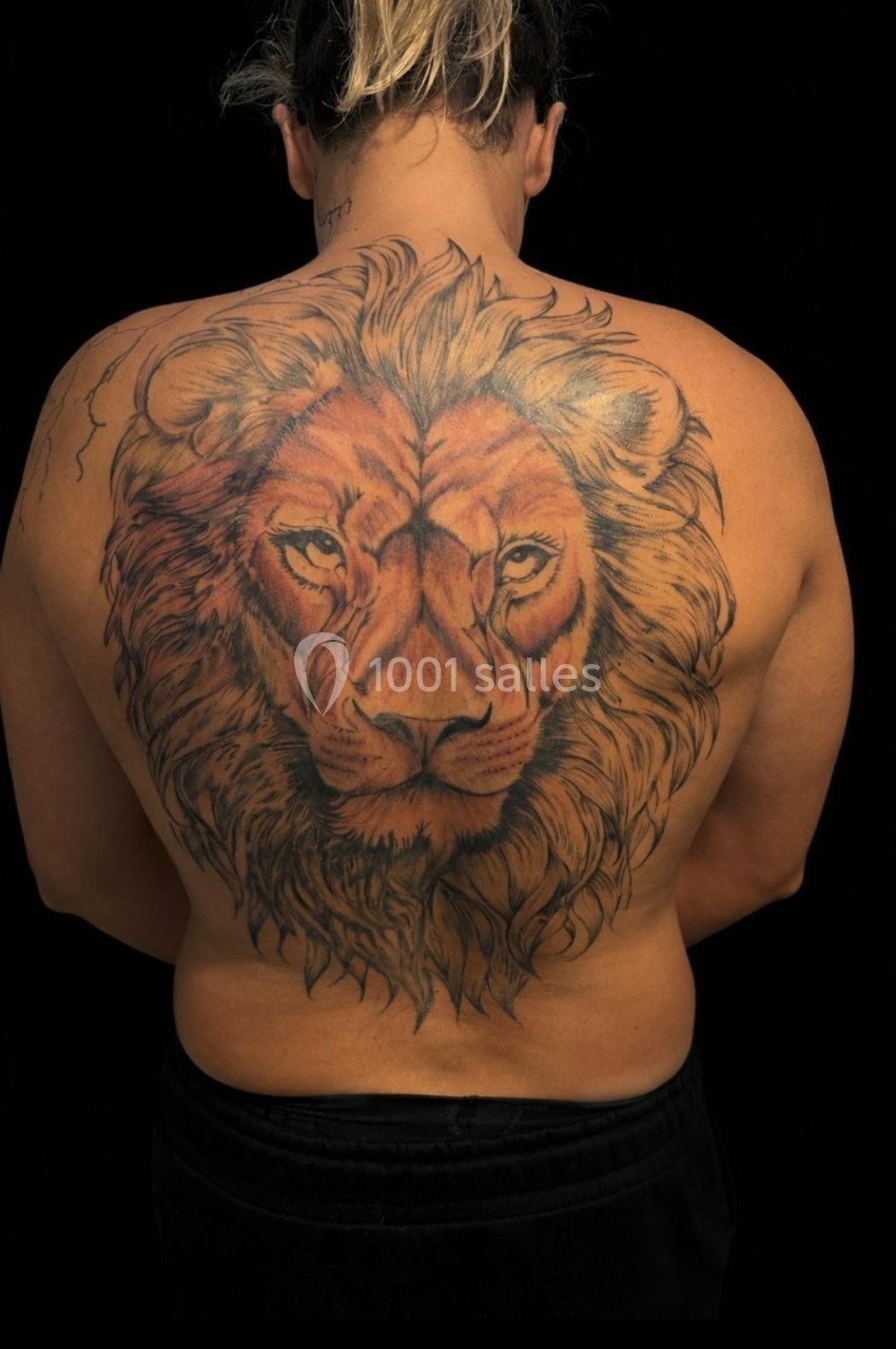 Tatouage détaillé d'un lion couvrant tout le dos d'une personne, sur fond noir.