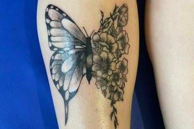 Tatouage sur une jambe représentant un papillon dont une aile se transforme en un bouquet de fleurs détaillées.