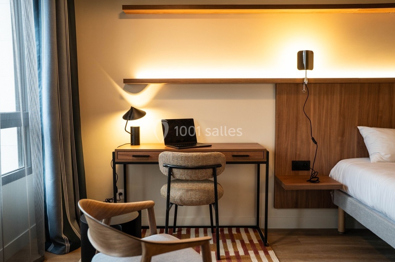 Bureau en bois avec lampe, ordinateur portable et chaise, dans une chambre moderne éclairée par une lumière chaude.